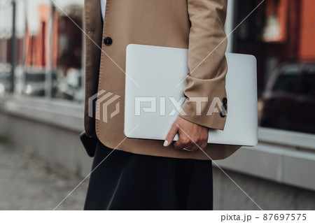 CloseUp Business Woman in a Brown Jacket Holding Laptop Outdoors 87697575