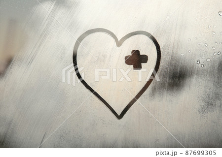 drawn shape of heart with bandage covering wound on foggy glass window raindrops 87699305