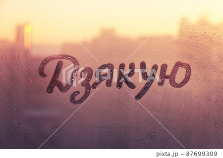 Ukrainian language word thanks in english are painted on wet orange sunrise glass of window 87699309
