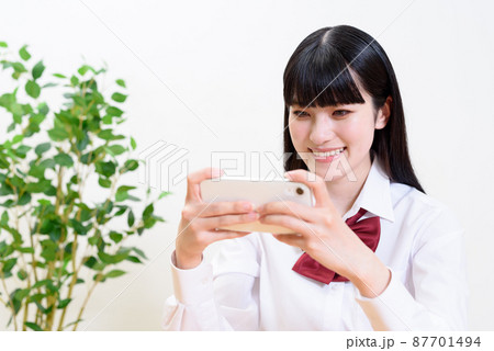 スマートフォンを横に持ってアプリゲームを操作する女子高校生　動画視聴　 87701494