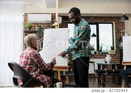 African american art teacher explaining draw illustration to senior woman 87702943