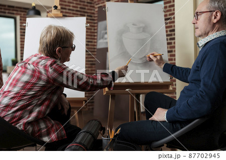 Elderly teacher explaining illustration lesson to student during art course 87702945
