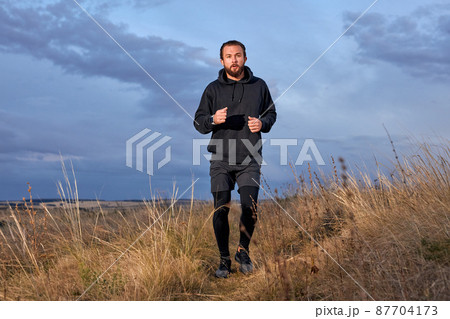 Athlete Strong Male Running Through the field. Man Wearing Black sportive wear Athlete Strong Male Running Through the field. Man Wearing Black sportive wear 87704173