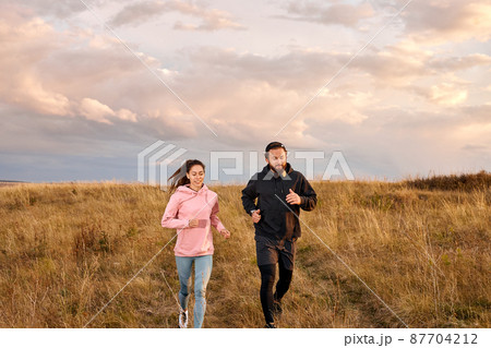 Young Couple Running On Field In Morning. Caucasian Man And Woman On Jogging Workout Young Couple Running On Field In Morning. Caucasian Man And Woman On Jogging Workout 87704212