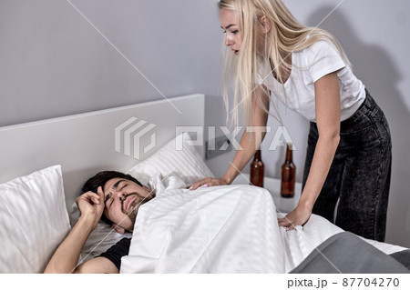 young married couple quarreled over alcohol addiction. woman stands above sleeping man young married couple quarreled over alcohol addiction. woman stands above sleeping man 87704270