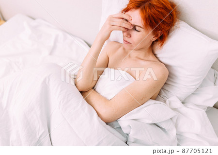 Portrait of a young sad tired woman lying in bed. Illness and headache 87705121