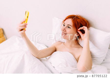 Portrait of a young beautiful redhead woman talking on the phone in bed Portrait of a young beautiful redhead woman talking on the phone in bed 87705122
