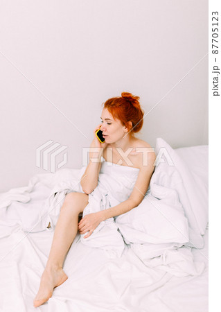 Portrait of a young beautiful redhead woman talking on the phone in bed Portrait of a young beautiful redhead woman talking on the phone in bed 87705123