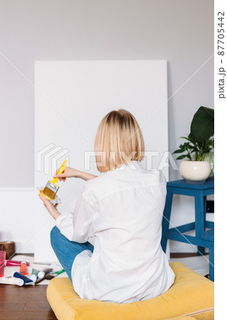 Young woman artist is painting at home in a creative studio setting.  87705442