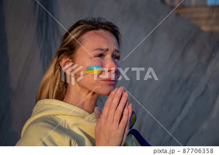 Ukrainian woman with a flag on the cheek crying  87706358