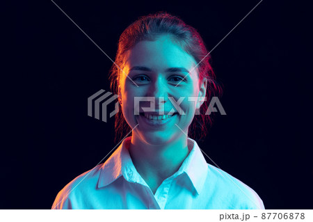 Half-length portrait of young pretty girl in white shirt isolated on dark background in blue neon light, filter. Concept of emotions, fashion, youth Half-length portrait of young pretty girl in white shirt isolated on dark background in blue neon light, filter. Concept of emotions, fashion, youth 87706878