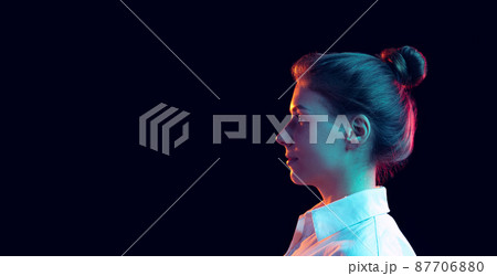 Profile view of young pretty girl in white shirt isolated on dark background in blue neon light, filter. Concept of emotions, fashion, youth 87706880