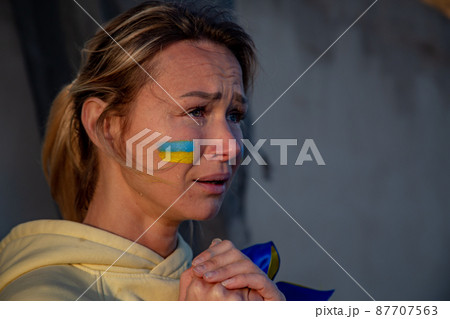Ukrainian woman with a flag on the cheek crying  87707563