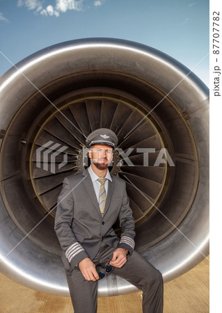 Bearded male pilot sitting in airplane engine at airport 87707782