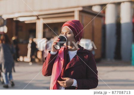 Young Arabic muslim woman in hijab walking at street seafront and drinking coffee take away Young Arabic muslim woman in hijab walking at street seafront and drinking coffee take away 87708713