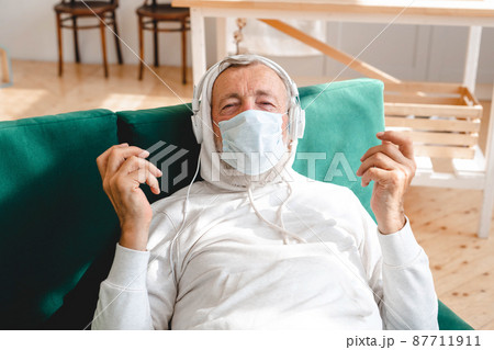 Senior man with medical mask on face using smartphone app for creating playlist music - Elderly male having fun with mobile phone technology - Tech and joyful elderly lifestyle concept 87711911