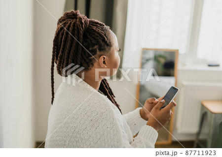 Portrait of African American female student dressed casually holding mobile phone and typing messages and communicating with friends via social networks using high-Internet connection. Portrait of African American female student dressed casually holding mobile phone and typing messages and communicating with friends via social networks using high-Internet connection. 87711923