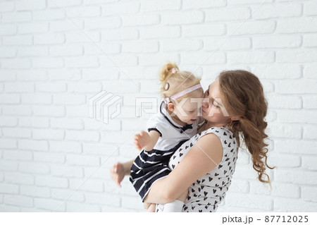 Mother holds her child with hearing aids and cochlear implants on white brick wall with copy space and place for advertising . Deaf and health concept Mother holds her child with hearing aids and cochlear implants on white brick wall with copy space and place for advertising . Deaf and health concept 87712025