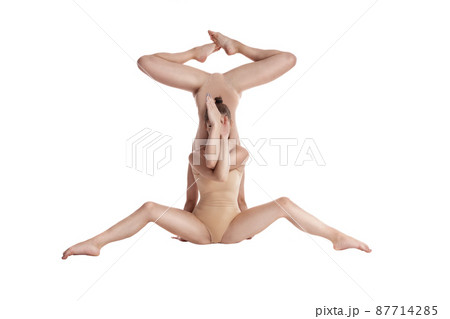Two flexible girls gymnasts in beige leotards performing complex elements of gymnastics using support, posing isolated on white background. Close-up. 87714285