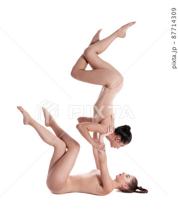 Two flexible girls gymnasts in beige leotards are performing exercises upside down using support and posing isolated on white background. Close-up. 87714309