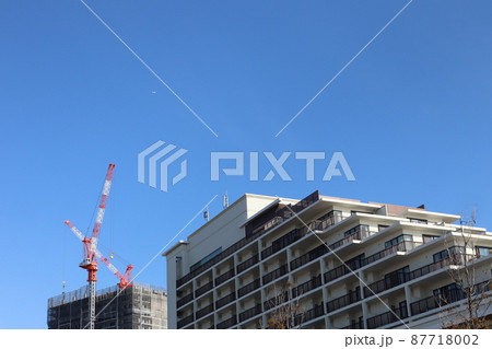青空と小さく飛行機のいる空とマンションとクレーンのある建設中のビルの見える街の風景 87718002