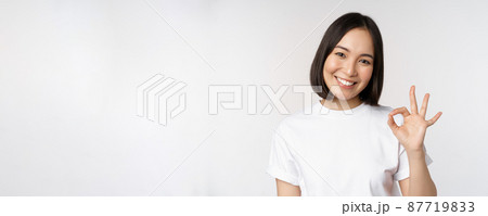 Everything okay. Smiling young asian woman assuring, showing ok sign with satisfied face, standing over white background 87719833