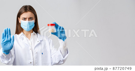 Covid-19, preventing virus, healthcare workers and quarantine concept. Serious concerned doctor in medical mask and PPE, tell to stop using this pills, showing bad medicine or antibiotics 87720749