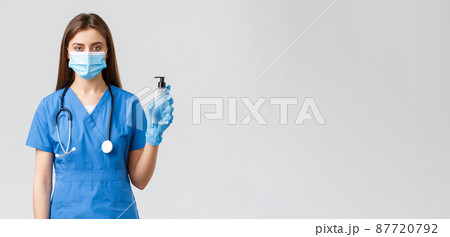 Covid-19, preventing virus, health, healthcare workers and quarantine concept. Serious female nurse in medical mask, scrubs and gloves fighting coronavirus, holding hand sanitizer Covid-19, preventing virus, health, healthcare workers and quarantine concept. Serious female nurse in medical mask, scrubs and gloves fighting coronavirus, holding hand sanitizer 87720792