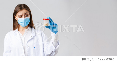 Covid-19, preventing virus, healthcare workers and quarantine concept. Unsure, curious doctor in scrubs and medical mask look intrigued and uncertain at container with medicine pills 87720987