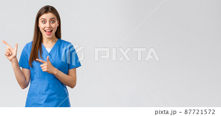 Healthcare workers, prevent virus, insurance and medicine concept. Surprised happy doctor or nurse in blue scrubs pointing finger left at great news, show information, banner or advertisement Healthcare workers, prevent virus, insurance and medicine concept. Surprised happy doctor or nurse in blue scrubs pointing finger left at great news, show information, banner or advertisement 87721572