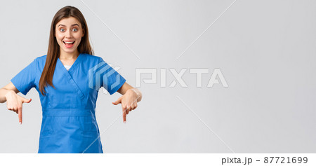 Healthcare workers, prevent virus, covid-19 test screening, medicine concept. Excited happy attractive nurse or doctor in blue scrubs, pointing fingers down, found great promo, showing banner 87721699