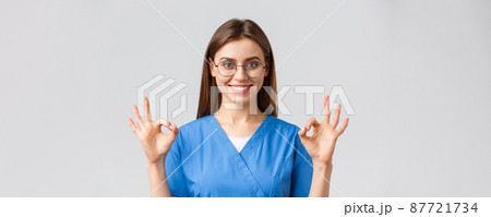 Healthcare workers, medicine, insurance and covid-19 pandemic concept. Confident and optimistic female nurse, doctor in blue scrubs and glasses, show okay sign, guarantee best service quality Healthcare workers, medicine, insurance and covid-19 pandemic concept. Confident and optimistic female nurse, doctor in blue scrubs and glasses, show okay sign, guarantee best service quality 87721734