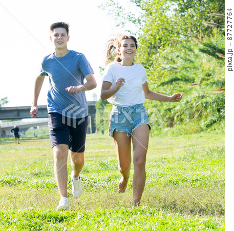 Laughing teenagers playing outdoors funning at grass on day 87727764