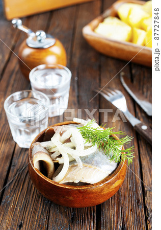 bowl of salted herring on the background of a glass of vodka and decanter. Salted herring in jar as a snack for vodka. 87727848