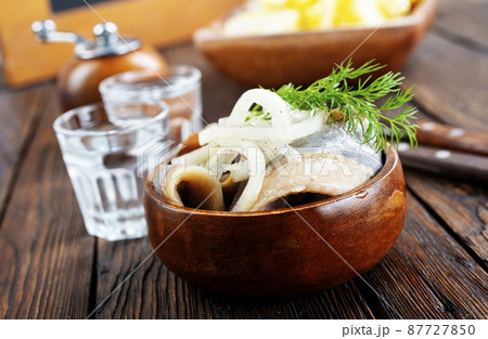 bowl of salted herring on the background of a glass of vodka and decanter. Salted herring in jar as a snack for vodka. 87727850