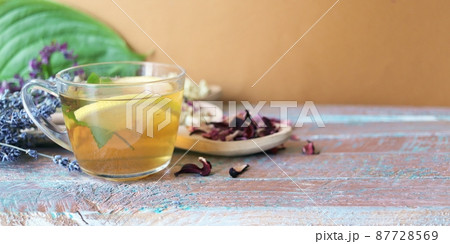 Cup of green tea with mint and lemon, dry petals of useful plants on a wooden table 87728569