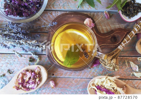 Cup of green tea with mint and lemon, dry petals of useful plants on a wooden table 87728570