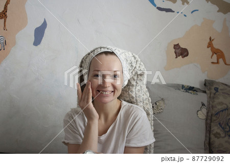An attractive happy woman of thirty years smears her cheeks with cream, a towel on her head, a home beauty ritual every day An attractive happy woman of thirty years smears her cheeks with cream, a towel on her head, a home beauty ritual every day 87729092