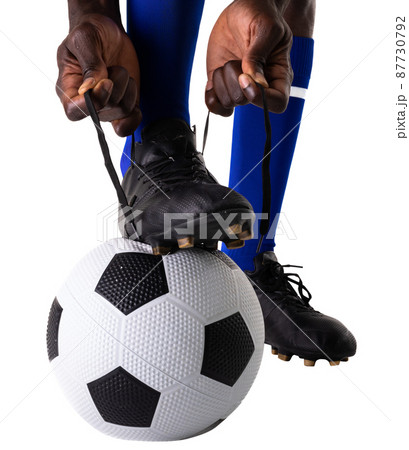 Low section of african american male soccer player tying shoelace on ball against white background Low section of african american male soccer player tying shoelace on ball against white background 87730792