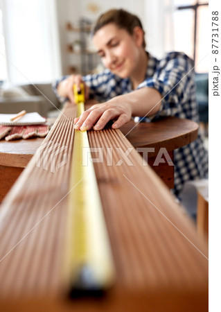 woman with ruler measuring wooden board at home 87731788