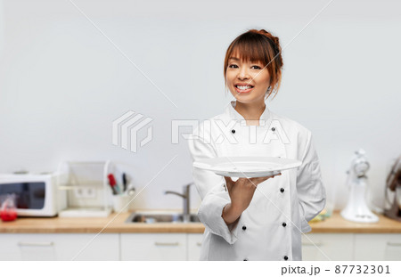 happy female chef holding empty plate on kitchen 87732301