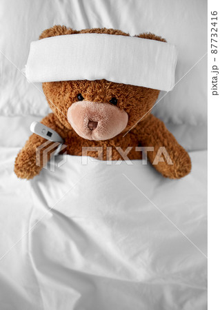 ill teddy bear with bandage and thermometer in bed ill teddy bear with bandage and thermometer in bed 87732416
