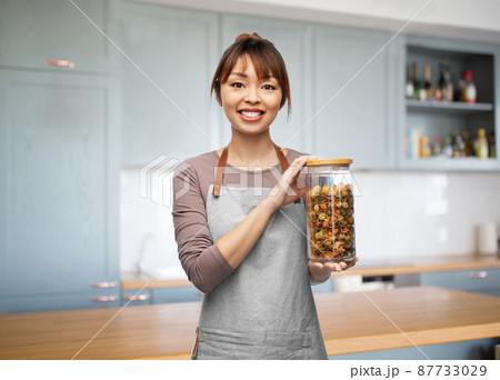 woman in apron holding jar with pasta at kitchen woman in apron holding jar with pasta at kitchen 87733029