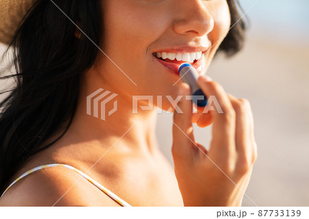 smiling woman in bikini with lip balm on beach 87733139