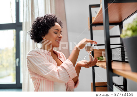 smiling woman with hourglass at shelf at home 87733159