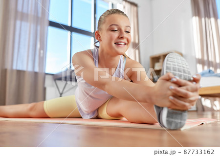 happy teenage girl exercising on yoga mat at home 87733162