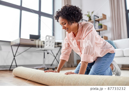 young woman unfolding carpet at home 87733232