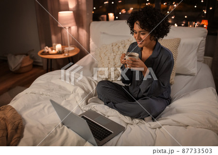 woman with laptop and mug sitting in bed at night 87733503