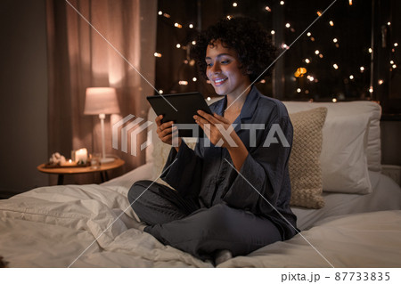 happy woman with tablet pc sitting in bed at night happy woman with tablet pc sitting in bed at night 87733835