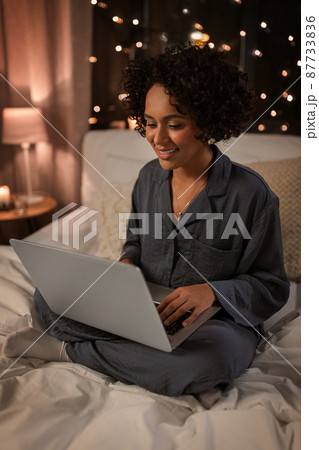 happy woman with laptop sitting in bed at night happy woman with laptop sitting in bed at night 87733836